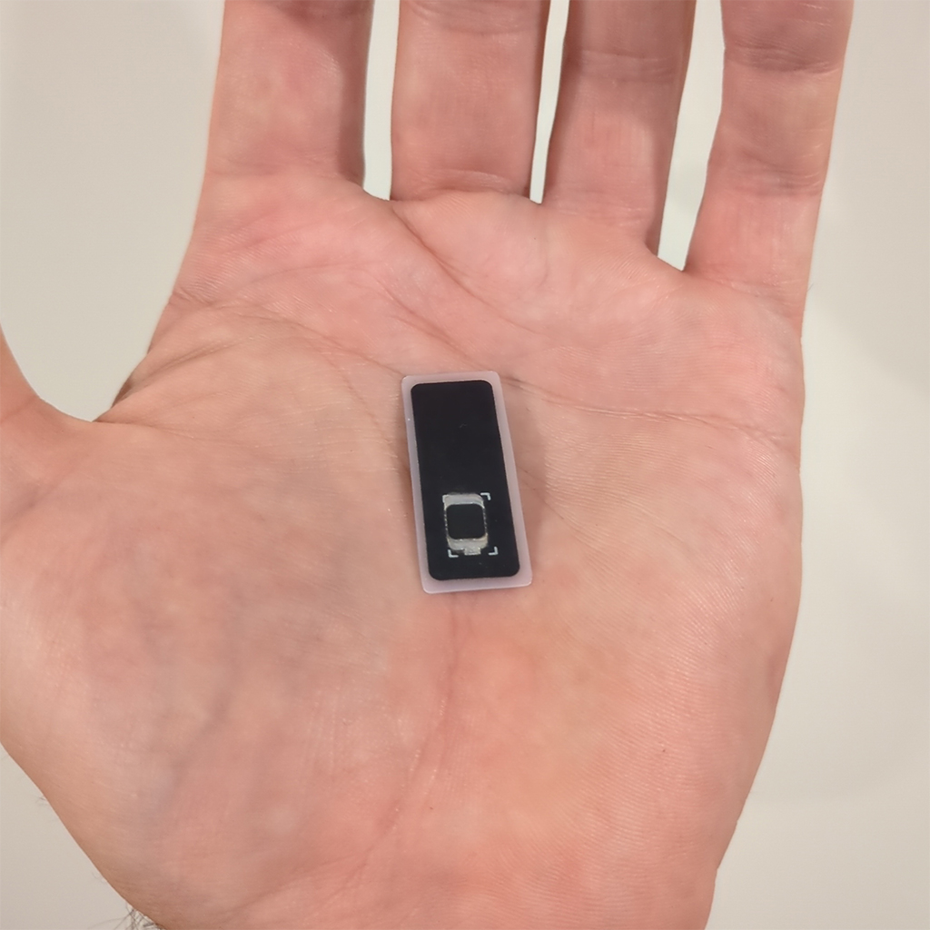 Apex Module held flat on an open palm: a wider rounded black biopolymer tile