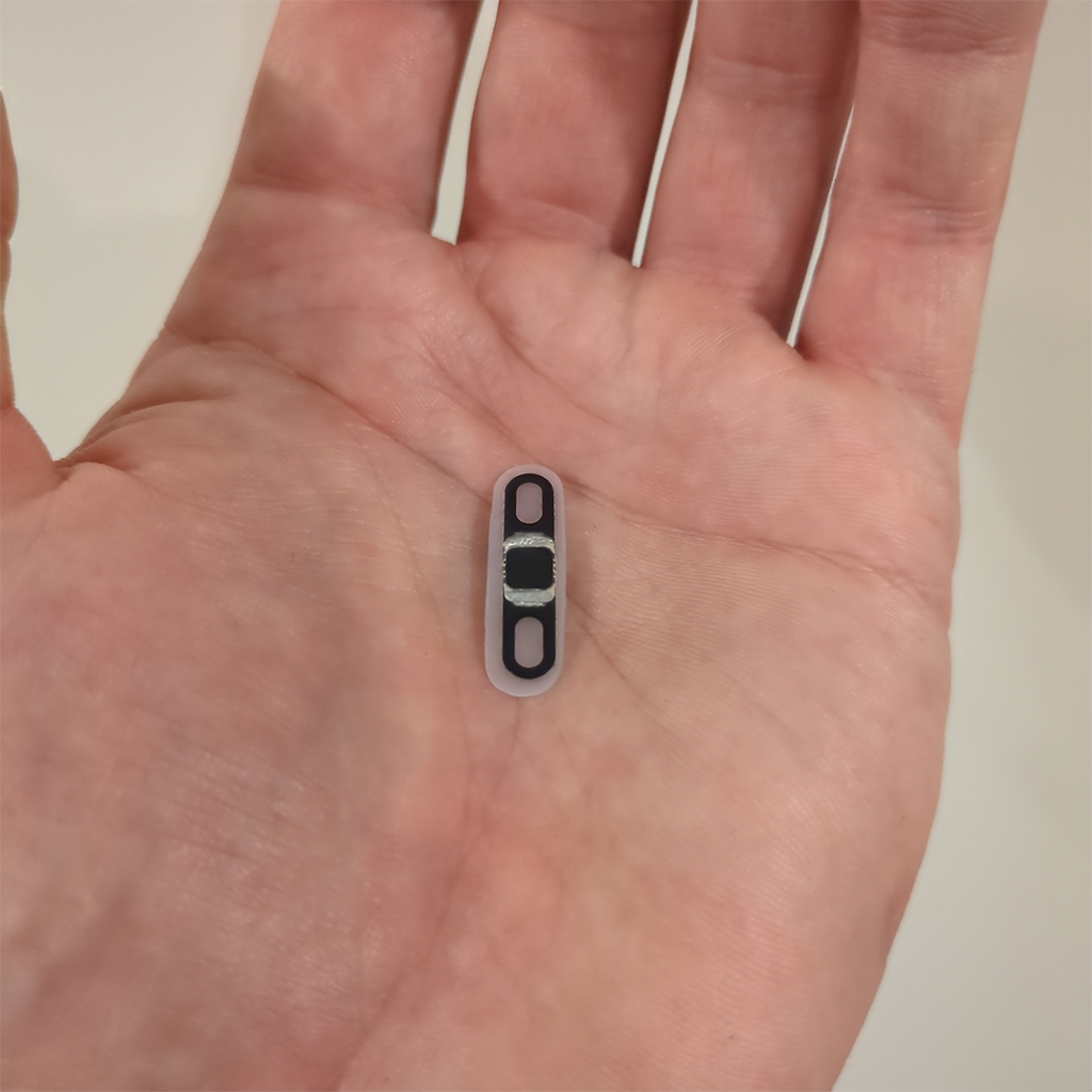 Apex Narrow held flat on an open palm: a thin black biopolymer strip about the length of a fingernail