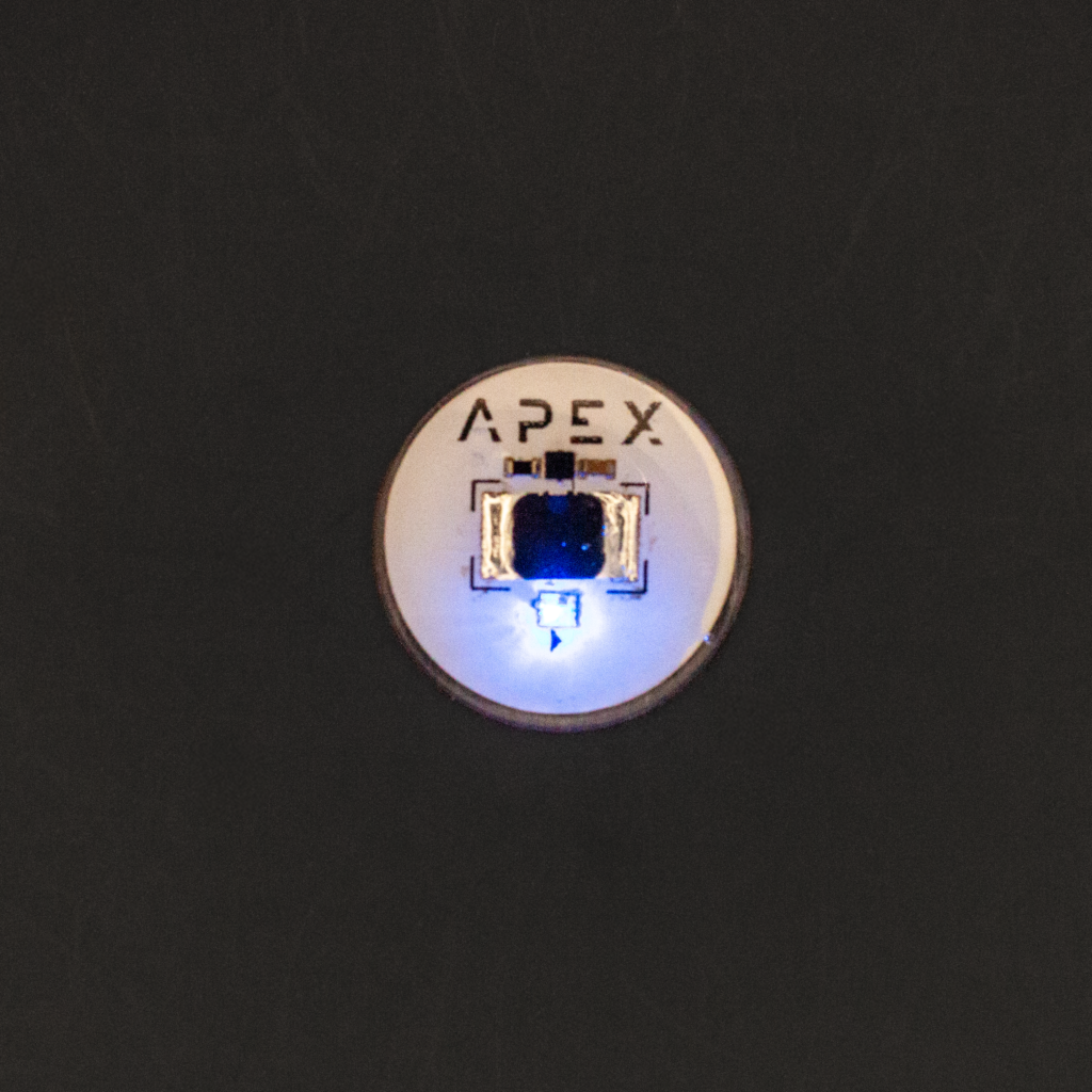 Apex Spectrum on a dark ground: a round implant with a copper rim and APEX lettering, its blue light lit