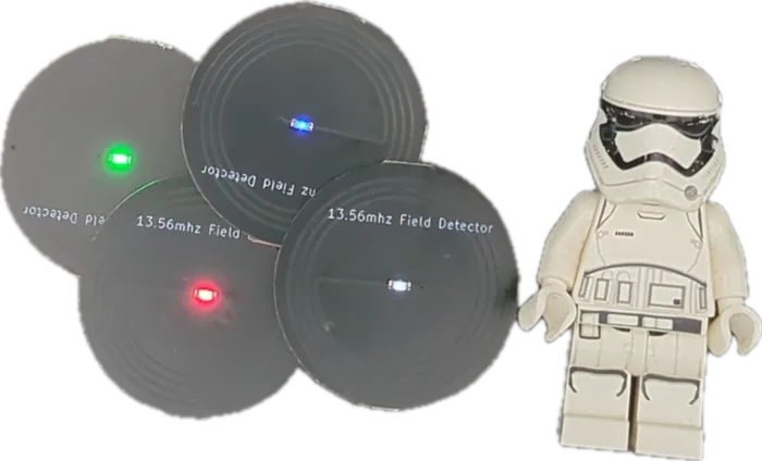 Four 27mm field detector discs in green, red, blue and white beside a LEGO stormtrooper minifigure for scale