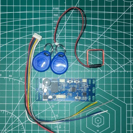 xEM Access Controller kit on a cutting mat: blue controller board, wiring harness, antenna coil and two 125kHz keyfobs