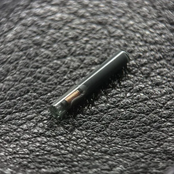 黒いレザーの上に置かれたガラスカプセル型インプラントSpark 2。ガラス越しに内部の黒いコアとアンテナの巻線が見える